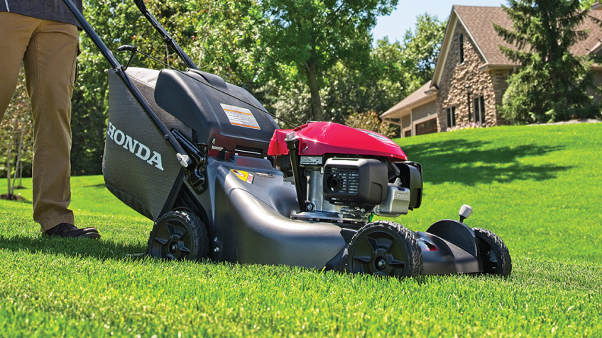 A person pushes a mower in a residential backyard.  