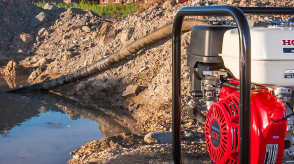 A Honda pump is being used to empty a pit filled with water. 	