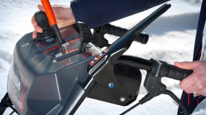 Closeup of a man's hands using the electronic chute joystick control on the handlebar-mounted console on a snowblower.  